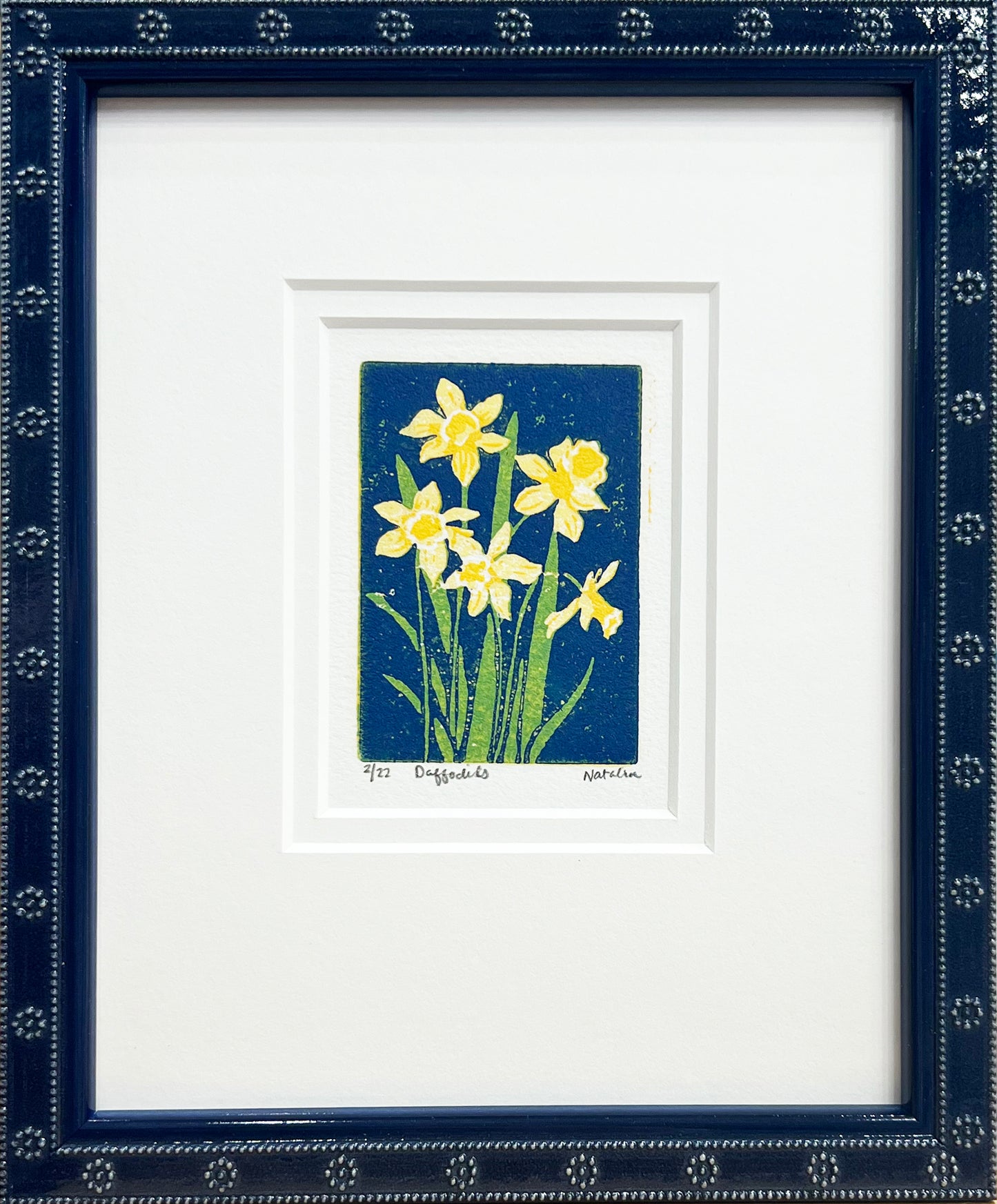 Daffodils is a 2"x3" four-color reduction block print inspired by the joyful spring blooms. Matted with a soft white double mat and framed in a lacquered blue frame with daisy embellishments.