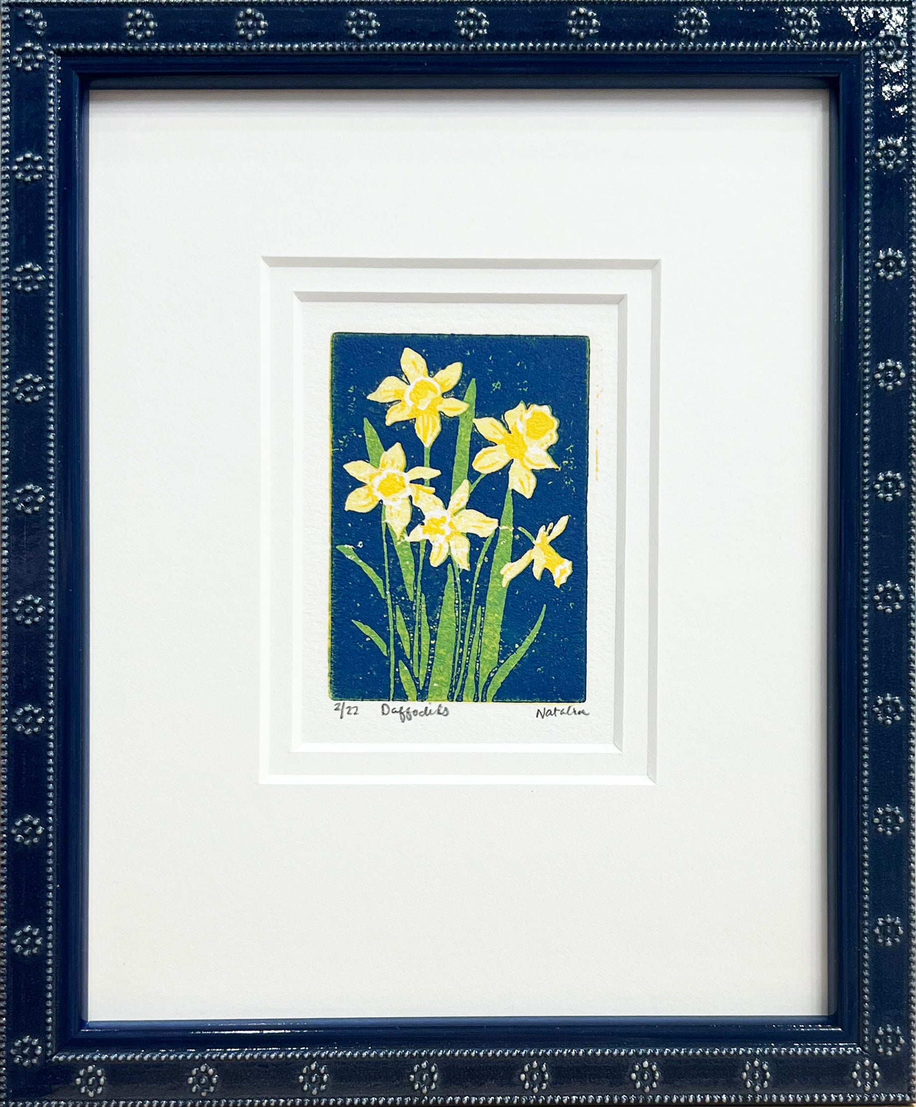 Daffodils is a 2"x3" four-color reduction block print inspired by the joyful spring blooms. Matted with a soft white double mat and framed in a lacquered blue frame with daisy embellishments.