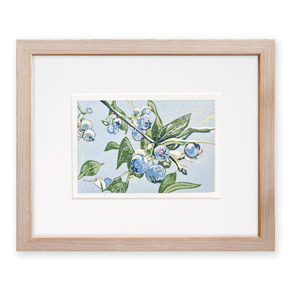 Framed artwork of blueberries and green leaves on a light blue background, with a light, cerused oak frame.