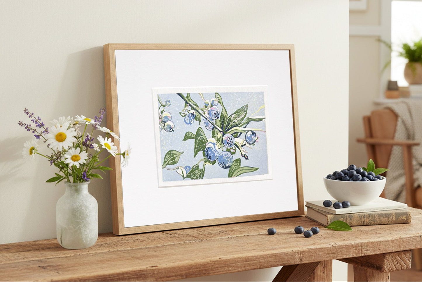 Framed blueberry block print on a wooden table with a vase of flowers and a bowl of berries.