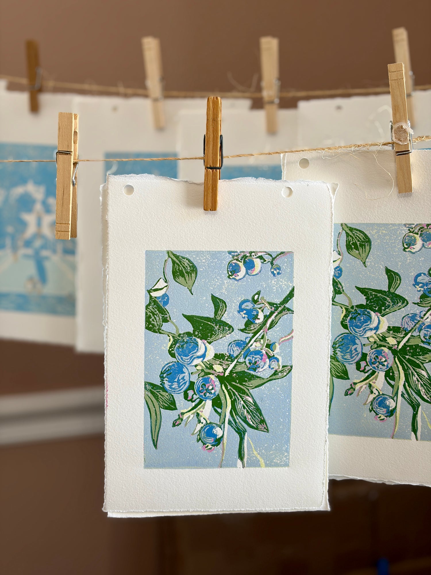 Block prints of blueberry plants hanging to dry on a line with wooden clips.