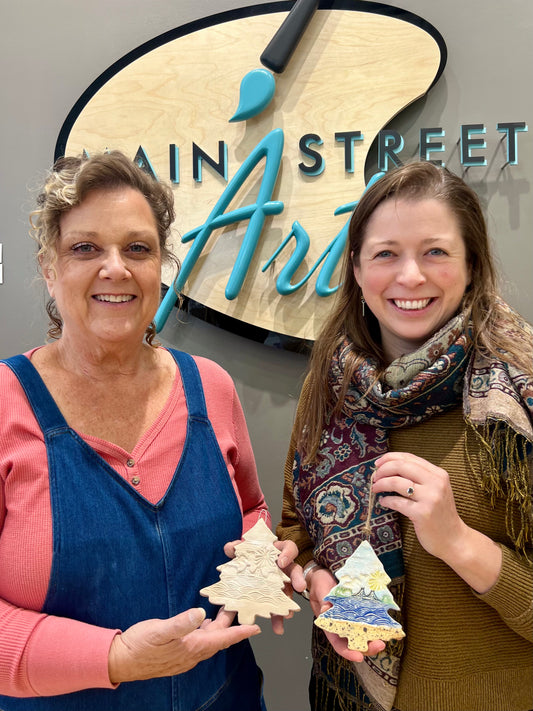 Jeanne DeHaan and Natalia Wohletz holding the 3" ceramic tree ornament featuring the Mackinac Bridge spanning the Great Lakes on a sunny day.