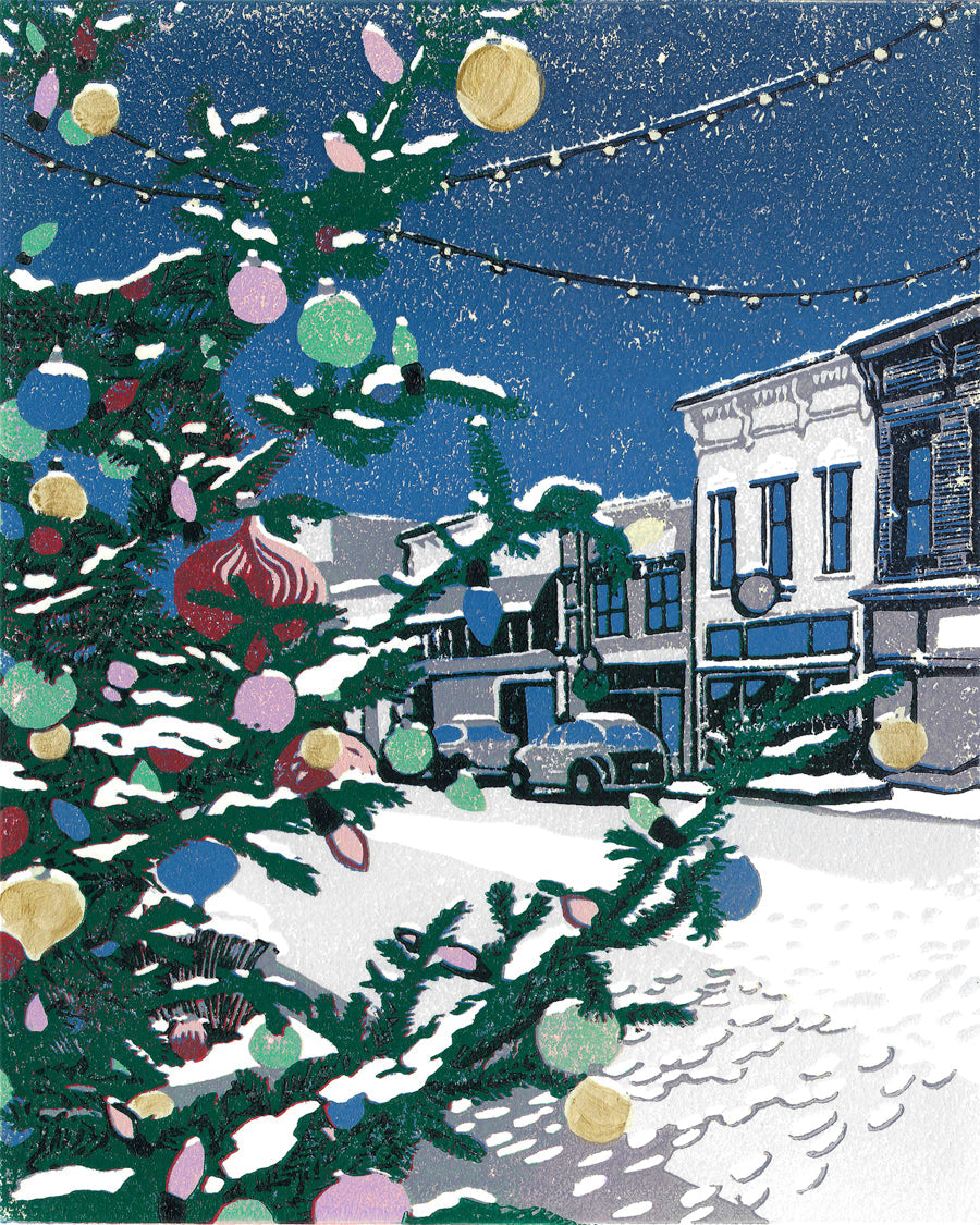 Small Town Christmas is a ten-color 8" x 10" block print of a charming scene of a Christmas tree lit up in the middle of a small downtown street. It exudes a cozy vibe when temperatures drop and Main Street is lit up for the holidays.