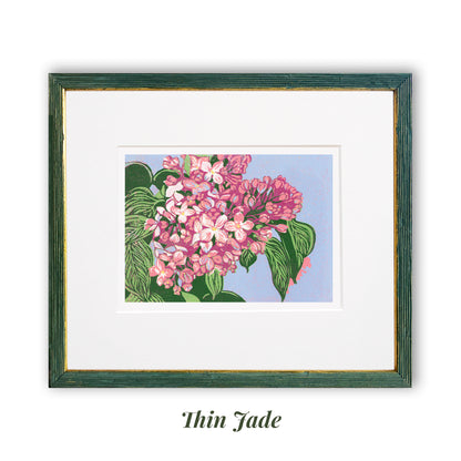 Reduction block print of blooming pink lilacs with olive green leaves against a periwinkle background. Matted in white and framed in a narrow jade and gold frame.