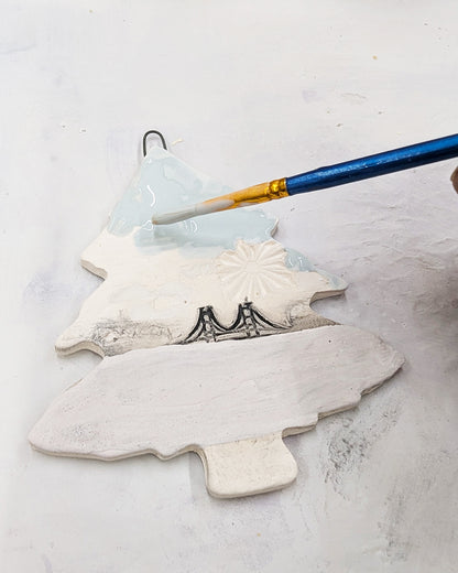 Decorative ceramic tree ornament being painted with a brush on a light background