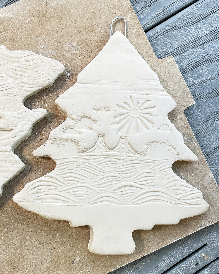 Unfinished ceramic Christmas tree ornament with embossed design on a textured surface.